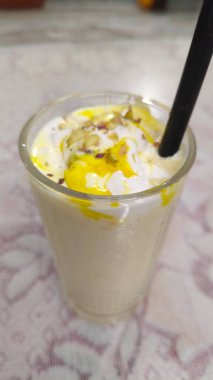 Bir bardak mango lassi, popüler bir Hint içeceği, resmedildi. Badem dilimleri (Prunus dulcis) ve safran iplikleri (Crocus sativus sativus) ile kaplı sarı renkli kremalı ve beyazdır.).