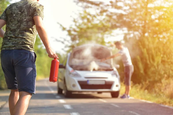 Brave man with fire extinguisher going to a car incident on the road with smoke on the engine