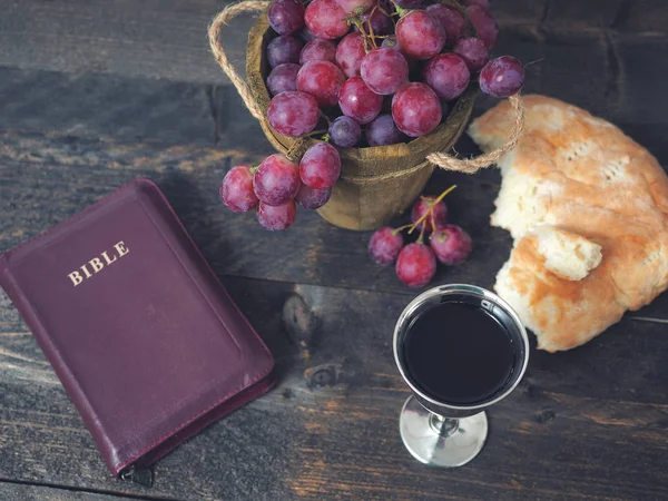 Homem partindo o pão, com vinho, uvas e Bíblia no fundo — Fotografia de Stock
