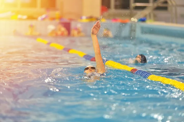 Menina em óculos e chapéu nadando na piscina de água azul — Fotografia de Stock