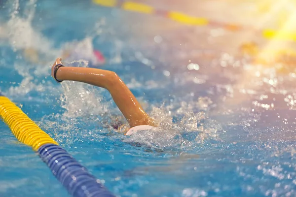 Молодий хлопчик у купальнику, окулярах та кепці плаває у басейні з блакитною водою — стокове фото