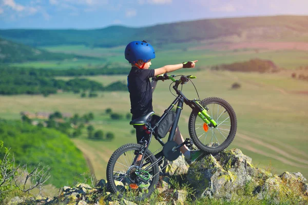 Little child stand next to his mountain bike on mountains edge and looks at the beautiful scenery — Stock Photo, Image