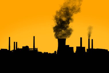Gün batımında açık turuncu gökyüzünde elektrik santrali siluetinin bacalarından çıkan siyah zararlı duman.. 