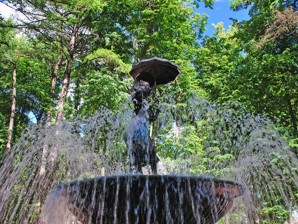 公園内の噴水 水の流れの中に傘を差した少女の姿 — ストック写真