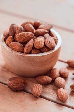 Ahşap kasedeki bademler ahşap masa arkasında.