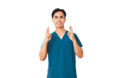 Mavi önlüklü gülümseyen genç Asyalı erkek hemşire ayakta durup kameraya bakarken şans ve umudun sembolü beyaz arka planda izole edilmiş bir şekilde el hareketi yapıyor..