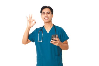 Önlüklü, steteskoplu, kendine güveni tam genç bir erkek hemşire elinde akıllı bir telefon tutuyor ve temiz beyaz bir arkaplanda izole edilmiş iyi bir jest gösteriyor..