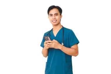 Mavi önlüklü ve steteskoplu genç erkek hemşire, akıllı telefon kullanıyor, temiz beyaz bir arka plana karşı güvenle duruyor, tıbbi veya sağlık hizmetleri kavramları için izole edilmiş..