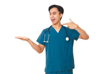 Steteskopla önlüklü heyecanlı genç erkek hemşire avucunun içini işaret ediyor. Reklamlar için boş bir alan gösteriyor. Temiz beyaz bir arka planda izole edilmiş..