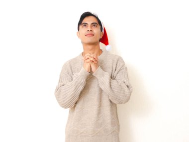 Gülümseyen Asyalı genç bir adam Noel Baba şapkası takıyor mutlu bir ifadeyle dua ediyor, beyaz arka planda izole edilmiş..