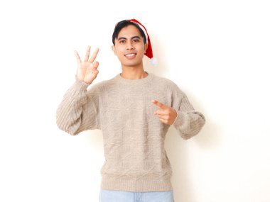 Gülümseyen Asyalı genç adam poz veriyor ve kendinden emin bir ifadeyle üç el hareketi gösteriyor, temiz beyaz arka planda izole edilmiş..