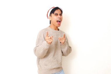 Noel Baba şapkası takan genç adam kameraya heyecanlı bir ifadeyle bakıyor, temiz beyaz bir arkaplan karşısında duruyor, festival ve tatil teması için mükemmel..