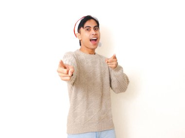 Noel Baba şapkası takan genç adam kameraya heyecanlı bir ifadeyle bakıyor, temiz beyaz bir arkaplan karşısında duruyor, festival ve tatil teması için mükemmel..