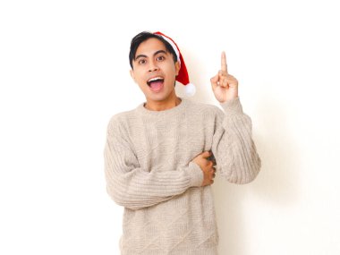Noel Baba şapkası takan heyecanlı genç adam temiz beyaz bir arkaplanda izole bir şekilde tatil sezonunu neşe ve enerjiyle kutluyor..
