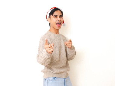 Noel Baba şapkası takan genç adam kameraya heyecanlı bir ifadeyle bakıyor, temiz beyaz bir arkaplan karşısında duruyor, festival ve tatil teması için mükemmel..