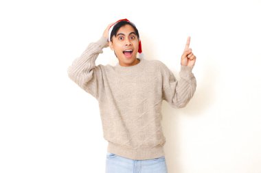 Noel Baba şapkası takan heyecanlı genç adam temiz beyaz bir arkaplanda izole bir şekilde tatil sezonunu neşe ve enerjiyle kutluyor..