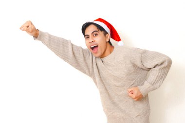 Genç adam Noel şapkası takmış, hareketli bir poz veriyor ve izole edilmiş beyaz arka planda mutlu bir ifade takınıyor, bayram ve kutlama konsepti için neşeli bir ruh hali içinde..