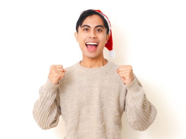 Noel şapkası takan genç adam başarıyı mutlu ve heyecanlı bir jestle kutluyor, beyaz arka planda izole edilmiş, neşeli bir tatil ifadesi var..