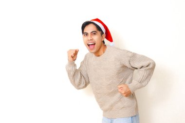 Genç adam Noel şapkası takmış, hareketli bir poz veriyor ve izole edilmiş beyaz arka planda mutlu bir ifade takınıyor, bayram ve kutlama konsepti için neşeli bir ruh hali içinde..