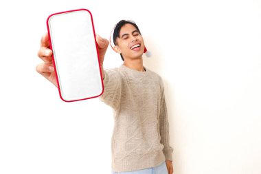 Genç Asyalı bir adam Noel şapkası takıyor. Beyaz izole edilmiş arka planda reklam ya da terfi için boş bir akıllı telefon model ekranı gösteriyor..
