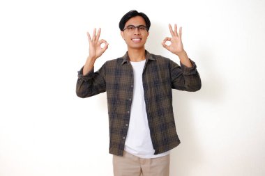 Heyecanlı Asyalı adam mutlu bir ifadeyle iyi bir el hareketi yapıyor, beyaz bir arka planda izole edilmiş.