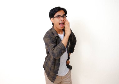 Heyecanlı Asyalı adam ayakta durup kameraya bakıyor, beyaz bir arka planda, eli ağızda sürpriz bir jest yapıyor.