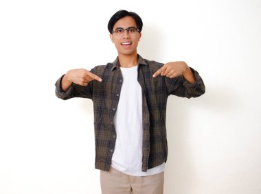 Heyecanlı genç Asyalı adam, beyaz arka planda izole edilmiş, mutlu bir ifadeyle aşağıya işaret ediyor.