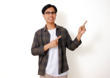 Heyecanlı genç Asyalı adam, izole edilmiş beyaz arka planda duruyor, gülümsüyor ve yanını işaret ediyor, neşeli bir ifade sergiliyor.