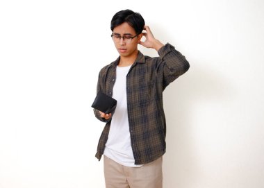 Asyalı üzgün genç bir adam, beyaz bir arka planda izole edilmiş, stresli bir ifadeyle boş bir cüzdanı tutuyor ve gösteriyor.