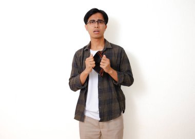 Asyalı üzgün genç bir adam, beyaz bir arka planda izole edilmiş, stresli bir ifadeyle boş bir cüzdanı tutuyor ve gösteriyor.