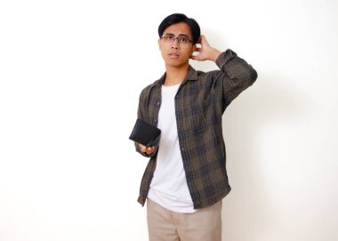 Asyalı üzgün genç bir adam, beyaz bir arka planda izole edilmiş, stresli bir ifadeyle boş bir cüzdanı tutuyor ve gösteriyor.