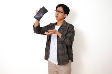 Asyalı üzgün genç bir adam, beyaz bir arka planda izole edilmiş, stresli bir ifadeyle boş bir cüzdanı tutuyor ve gösteriyor.