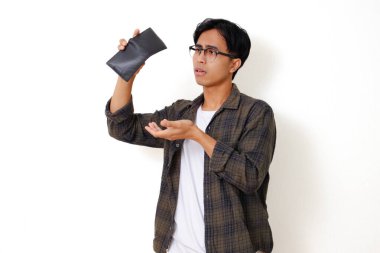 Asyalı üzgün genç bir adam, beyaz bir arka planda izole edilmiş, stresli bir ifadeyle boş bir cüzdanı tutuyor ve gösteriyor.