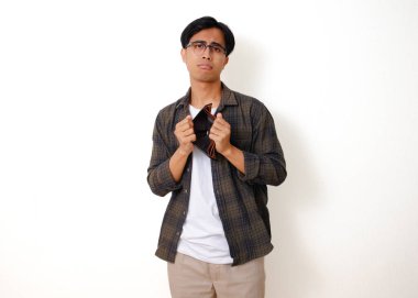 Asyalı üzgün genç bir adam, beyaz bir arka planda izole edilmiş, stresli bir ifadeyle boş bir cüzdanı tutuyor ve gösteriyor.