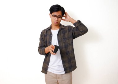 Asyalı üzgün genç bir adam, beyaz bir arka planda izole edilmiş, stresli bir ifadeyle boş bir cüzdanı tutuyor ve gösteriyor.