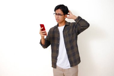 Kafası karışmış genç Asyalı adam telefonuna üzgün ve stresli bir ifadeyle bakıyor, temiz beyaz bir arka planda izole edilmiş..