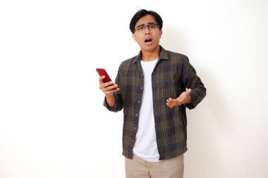 Kafası karışmış genç Asyalı adam telefonuna üzgün ve stresli bir ifadeyle bakıyor, temiz beyaz bir arka planda izole edilmiş..