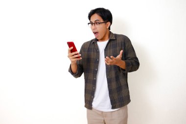 Mutlu, Asyalı genç bir adam, beyaz arka planda izole edilmiş, etkileyici bir yüz ifadesiyle cep telefonuna bakıyor.