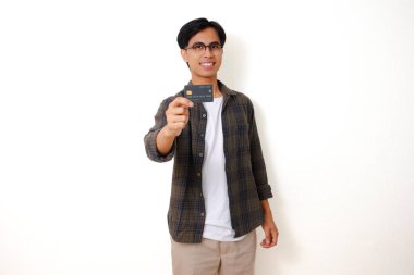 Gülümseyen Asyalı genç adam temiz beyaz bir arkaplanda izole edilmiş bir kredi kartı ürünü tutuyor ve gösteriyor.