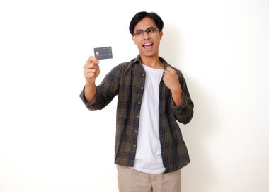 Gülümseyen Asyalı genç adam temiz beyaz bir arkaplanda izole edilmiş bir kredi kartı ürünü tutuyor ve gösteriyor.