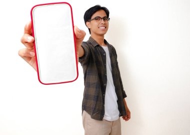 Heyecanlı genç Asyalı adam elinde boş bir cep telefonu ekranı ile başarıyı beyaz bir arka planda izole edilmiş neşeli bir hareketle kutluyor.
