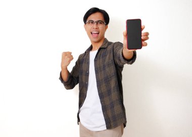 Heyecanlı genç Asyalı adam elinde boş bir cep telefonu ekranı ile başarıyı beyaz bir arka planda izole edilmiş neşeli bir hareketle kutluyor.