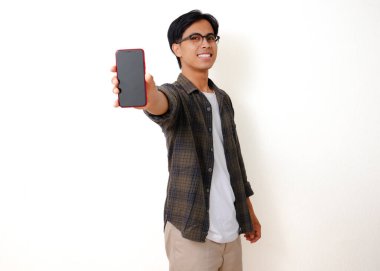 Heyecanlı genç Asyalı adam elinde boş bir cep telefonu ekranı ile başarıyı beyaz bir arka planda izole edilmiş neşeli bir hareketle kutluyor.