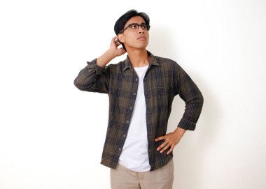 Stresli, genç Asyalı bir adam beyaz arka planda izole edilmiş, kafası karışmış bir ifadeyle başını kaşıyor.