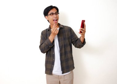 Elinde cep telefonu olan mutlu bir Asyalı adam heyecanlı bir ifadeyle bir video mesajı gösteriyor, beyaz arka planda izole edilmiş.