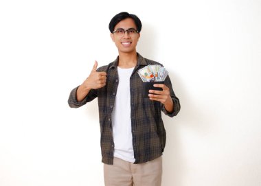 Gülümseyen Asyalı genç bir adam para dolu bir cüzdan taşıyor, mutluluk ve finansal başarı yayıyor. Temiz beyaz bir arkaplanda izole edilmiş.