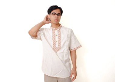 Kafası karışmış Endonezyalı Müslüman adam stresli bir ifadeyle ayakta duruyor, hayal kırıklığı içinde kafasını kaşıyor, beyaz arka planda izole edilmiş.