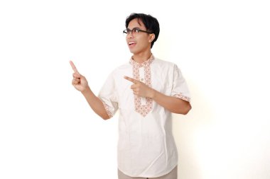 Geleneksel Müslüman gömlekli mutlu Endonezyalı adam beyaz arka planda izole bir şekilde ayakta duruyor ve onu işaret ediyor.