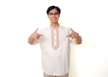 Mutlu, heyecanlı Endonezyalı Müslüman adam, beyaz arka planda izole bir şekilde dikilip işaret ediyor.