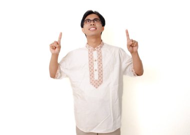 Mutlu, heyecanlı Endonezyalı Müslüman adam, beyaz arka planda izole edilmiş bir şekilde ayakta ve parmağıyla işaret ediyor.